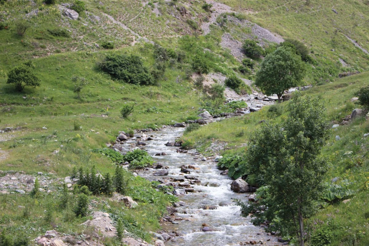 A small stream running down a green mountain valley